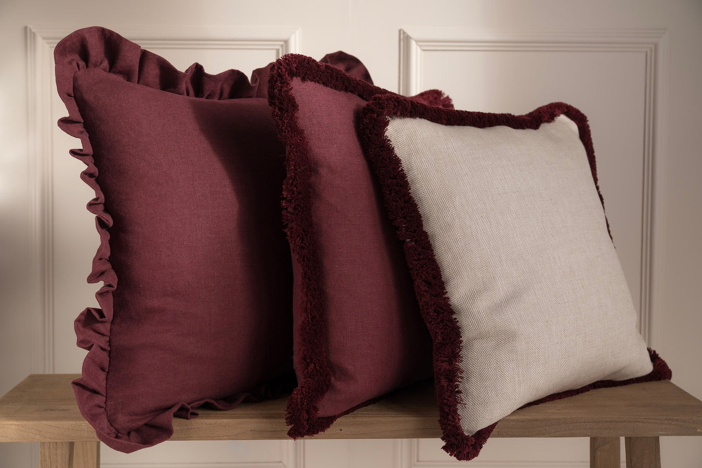 A stack of burgundy cushions on a bench. 100% Irish Linen. Made in Ireland
