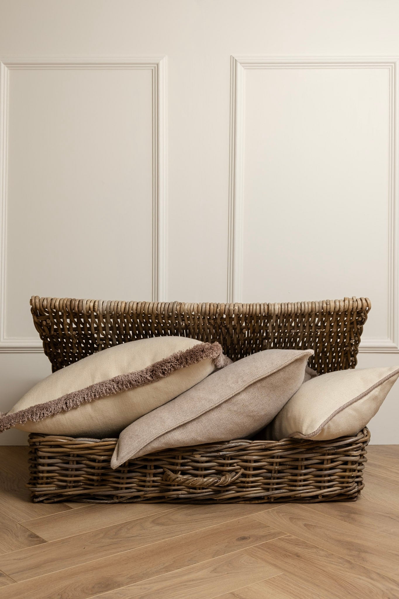 A set of neutral linen cushions with taupe fringe displayed in a wicker basket.
