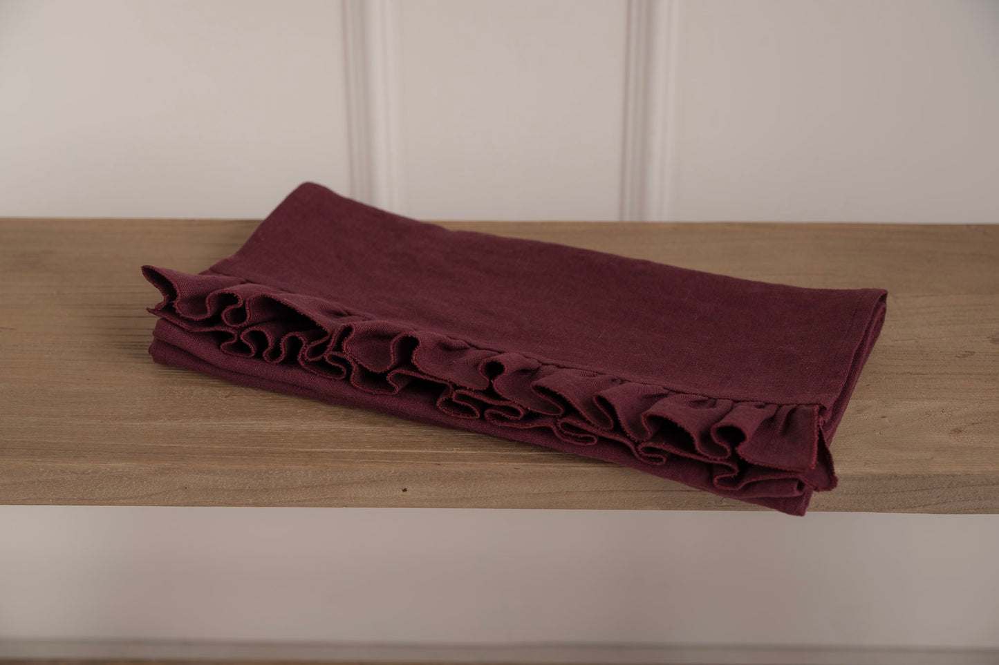 Folded burgundy fabric with ruffles on a wooden surface against a white wall.