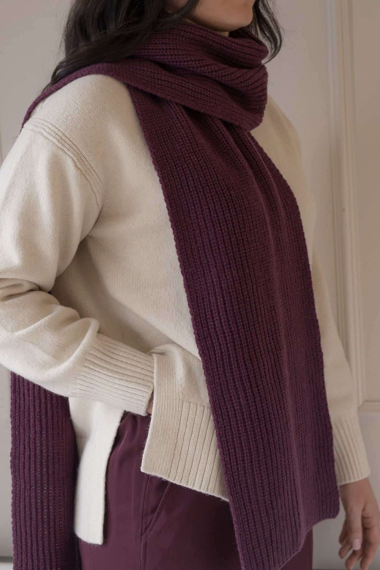 Person wearing a beige sweater and purple scarf with a neutral background