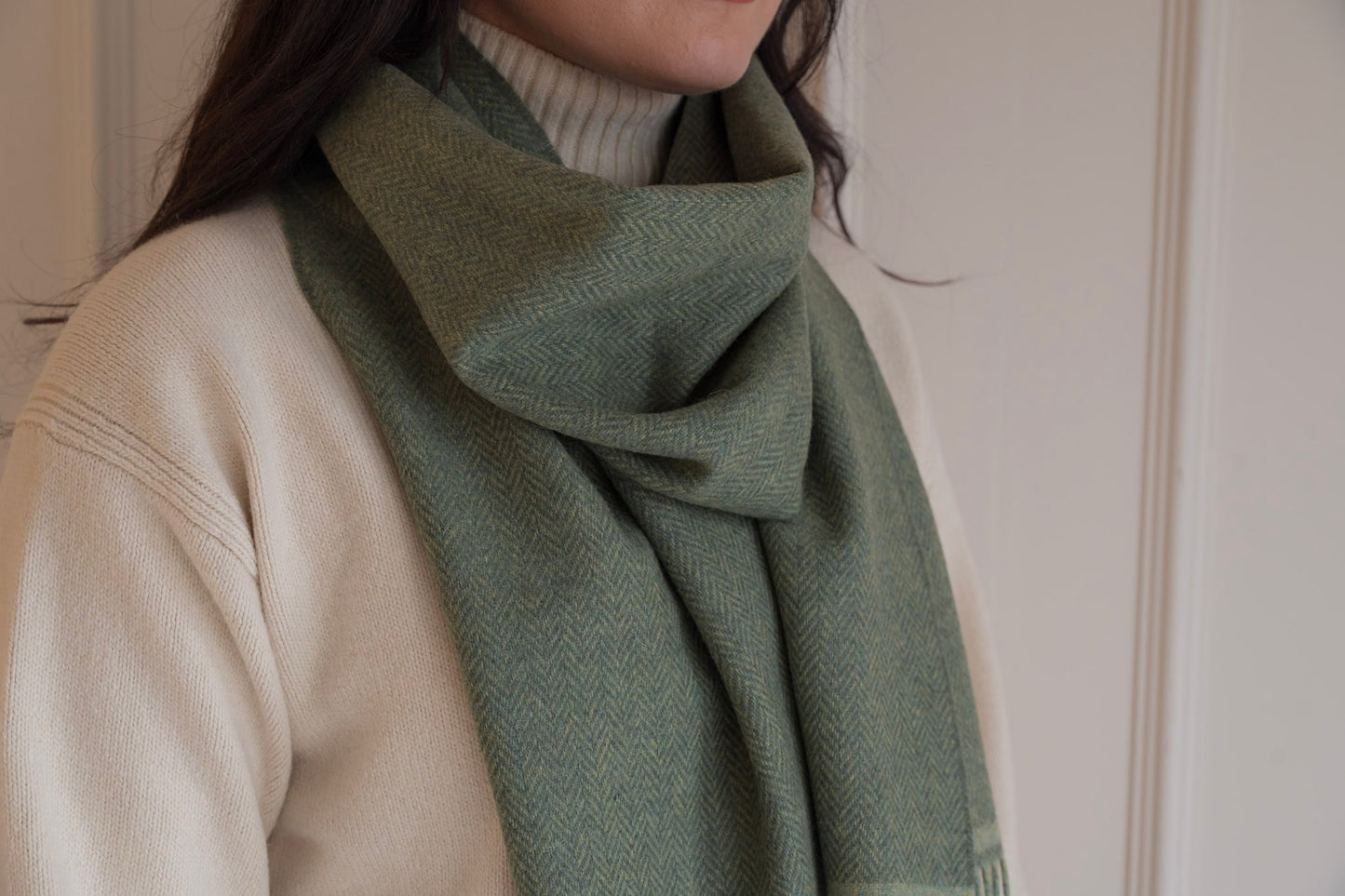 Person wearing a green scarf over a beige sweater against a neutral background