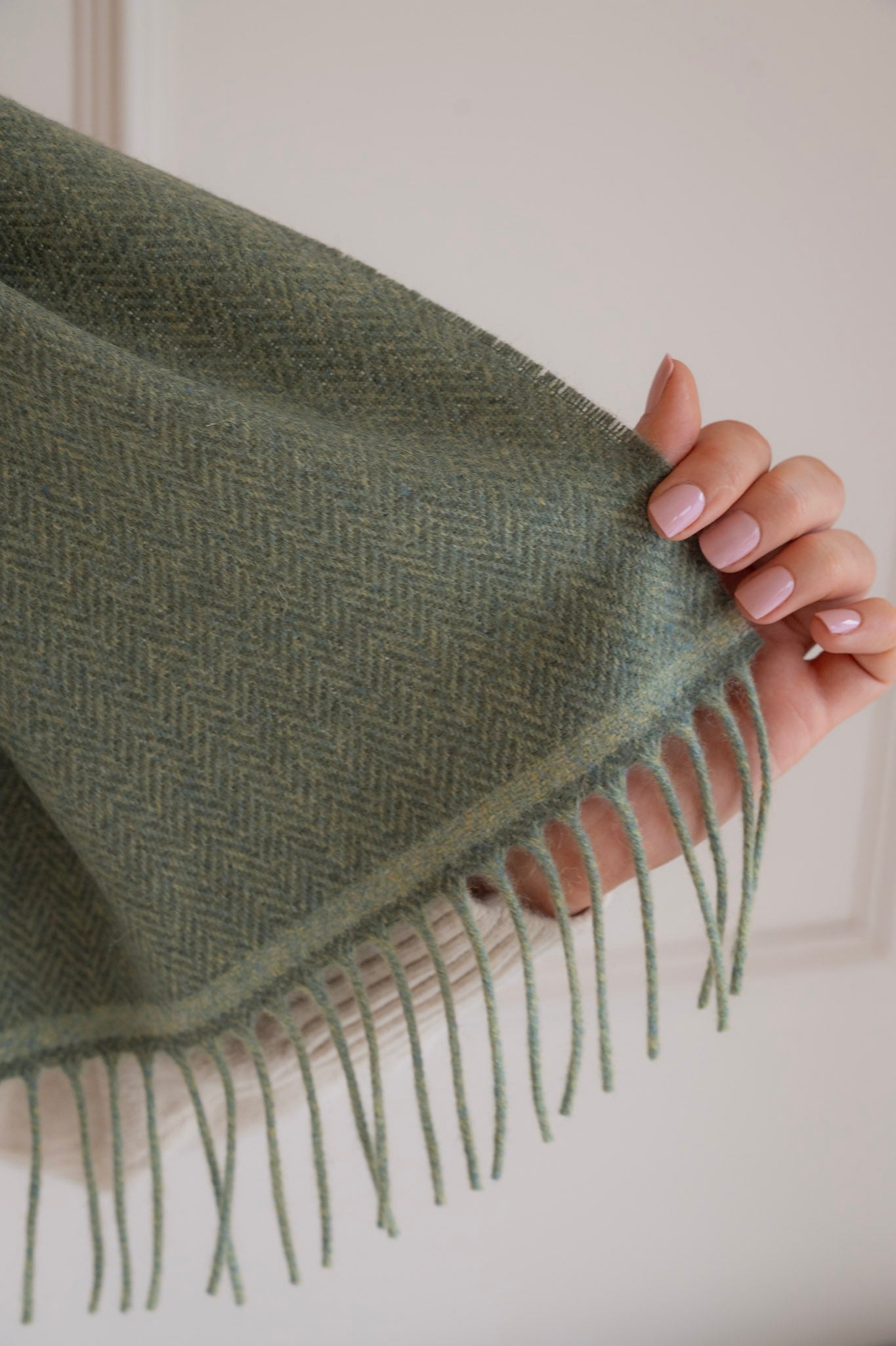 Green woven scarf with fringes held by a hand against a neutral background