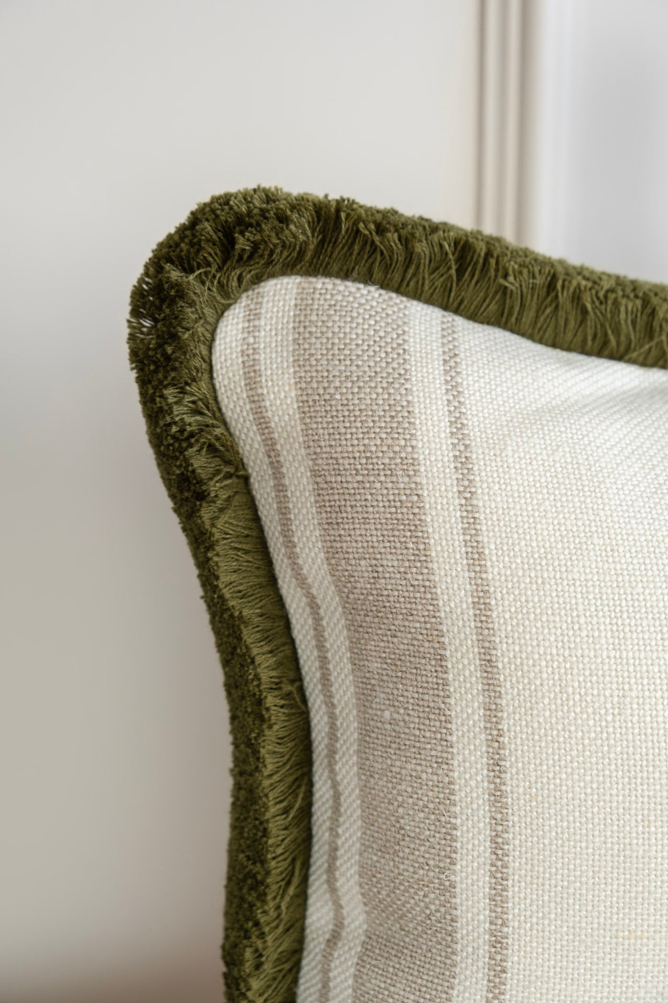 Close up of a neutral striped cushion with a deep olive fringe detail. Made in Ireland, 100% Linen