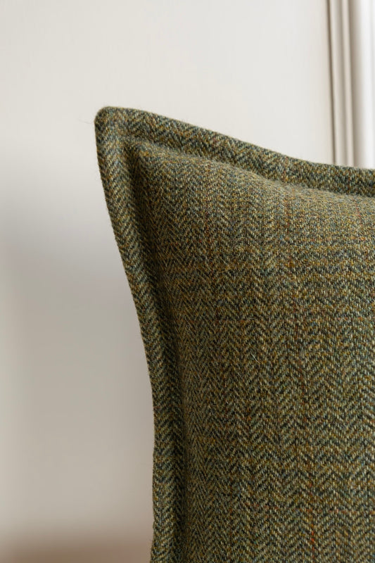 Green Tweed Cushion. Irish Tweed cushion. A close-up of a green tweed cushion with a herringbone and check pattern design, featuring a stitched border. Available in a Lumbar Bolter, or Square cushions. Woven and Made in Ireland.