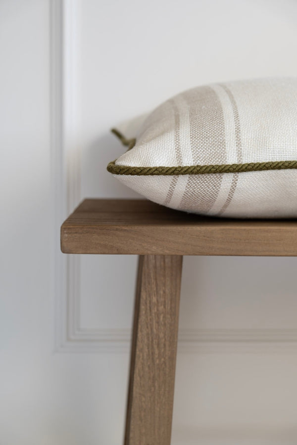 A cushion with a shadowed stripe pattern and deep olive green piping, displayed on a wooden bench. Made in Ireland.