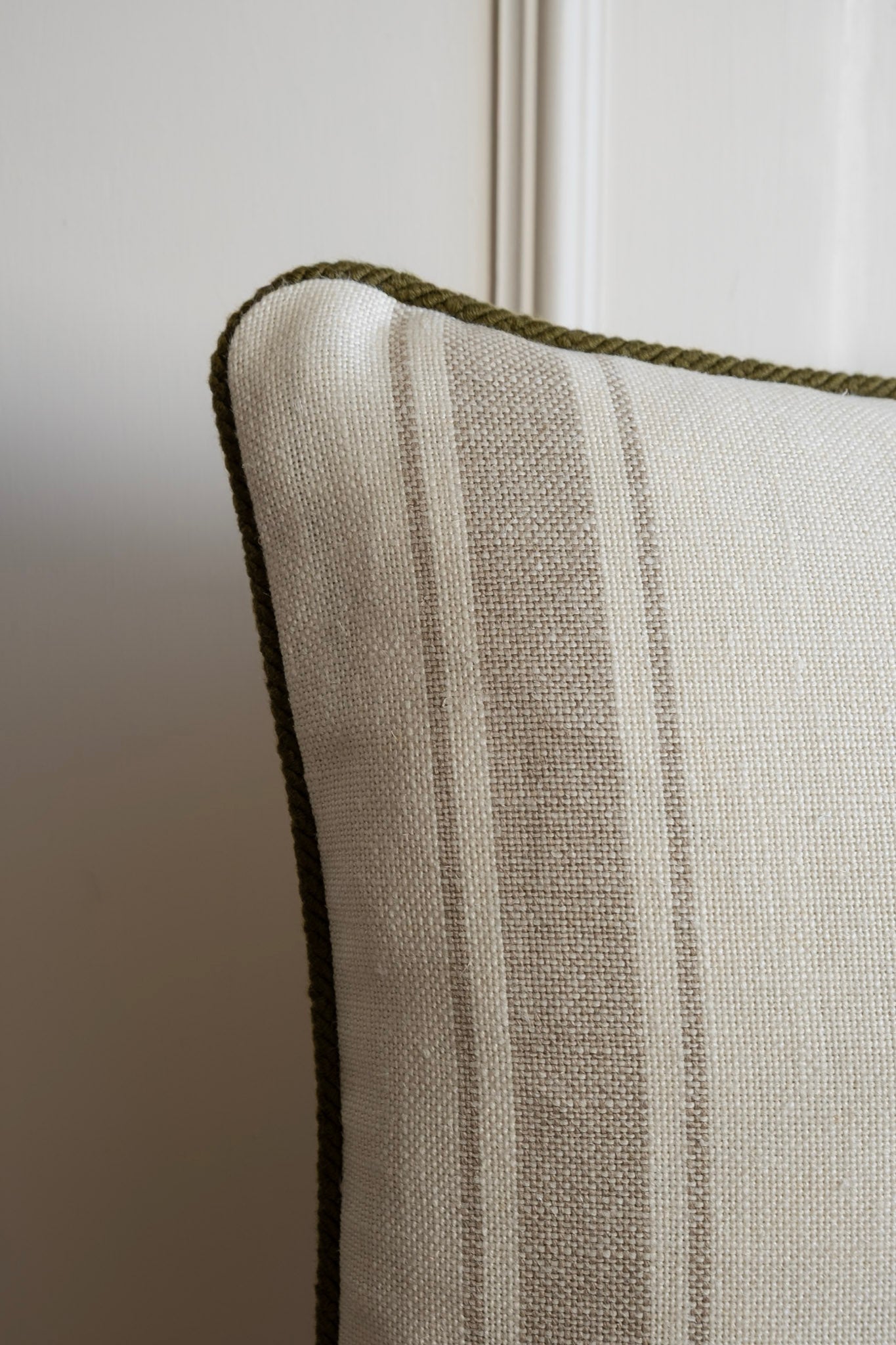 Close up of a neutral striped cushion with olive green piping. Made in Ireland. 